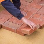 From above crop unrecognizable construction worker in uniform laying bricks on ground in daylight